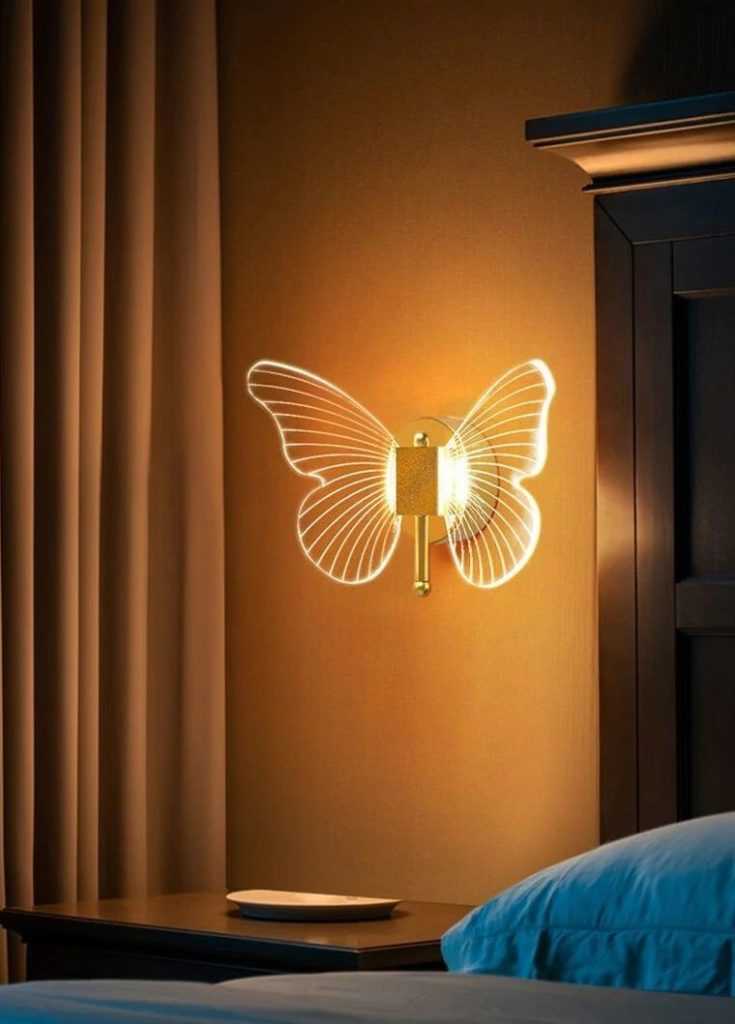 Arandela em formato de borboleta dourada, com iluminação nas asas finamente delineadas. A peça cria um efeito delicado e decorativo, ideal para ambientes aconchegantes como quartos.
