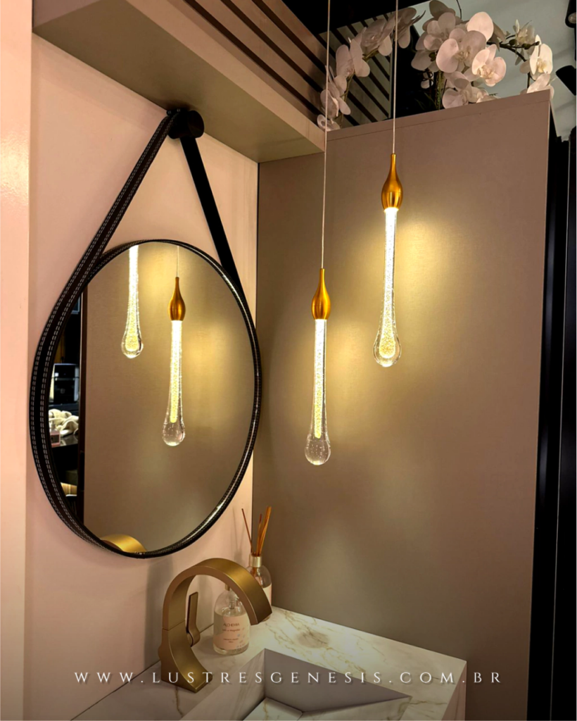 Lavabo com luminárias pendentes em formato de gotas douradas iluminadas, demonstrando a iluminação ideal para banheiros.