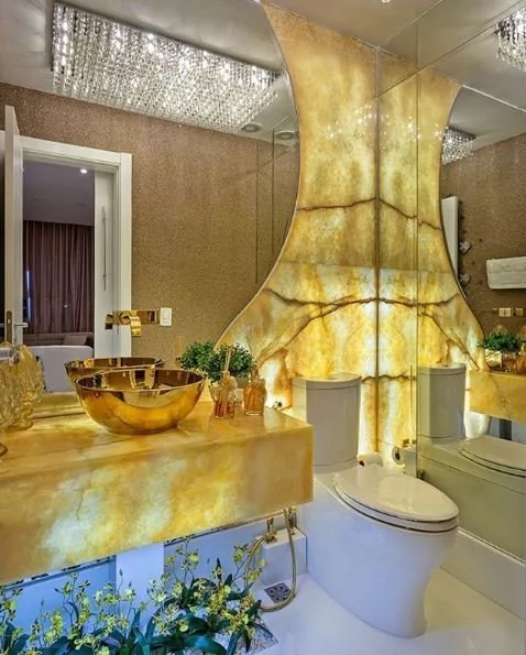 Lavabo luxuoso com parede e bancada de pedra iluminada em tons dourados, demonstrando a Iluminação para banheiros.
