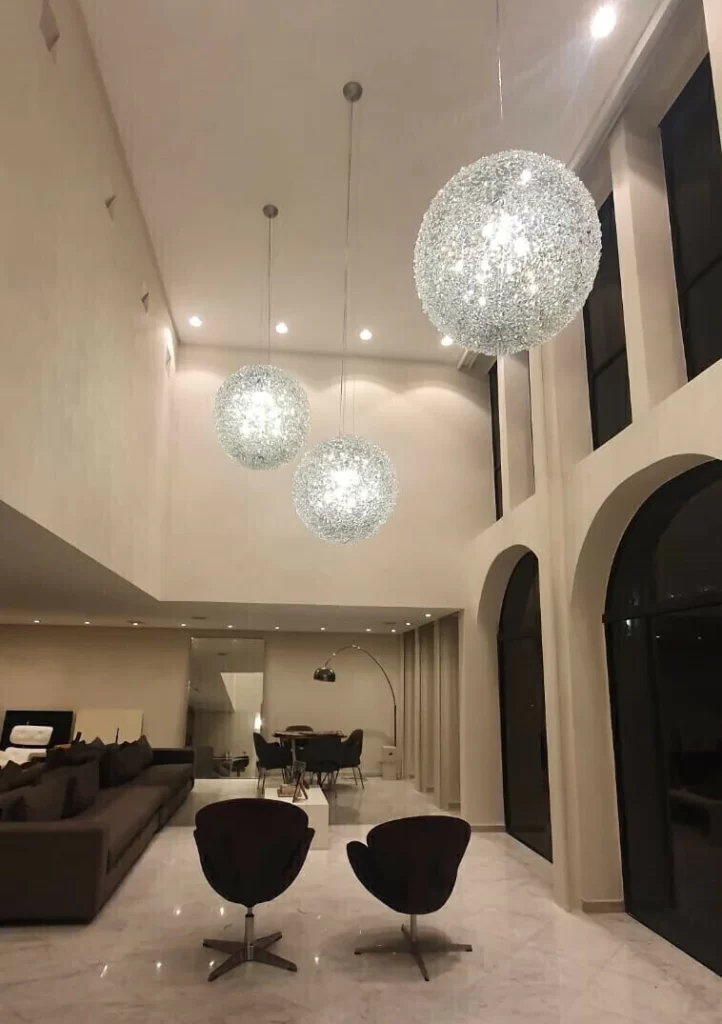 Três lustres esféricos brilham em sala ampla com pé-direito duplo.