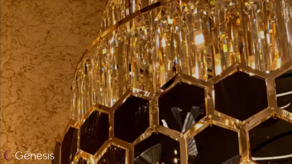 Lustre de cristal com estrutura dourada e design geométrico hexagonal, iluminado com luz quente, ideal para ambientes sofisticados como salas de jantar, halls e projetos de alto padrão.