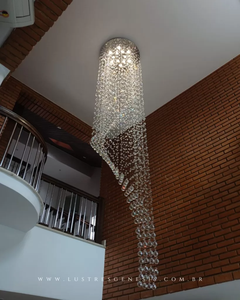 Lustre cascata de cristal para pé-direito duplo, com design assimétrico e cristais suspensos em fios formando efeito escultural, ideal para escadas e halls de entrada.