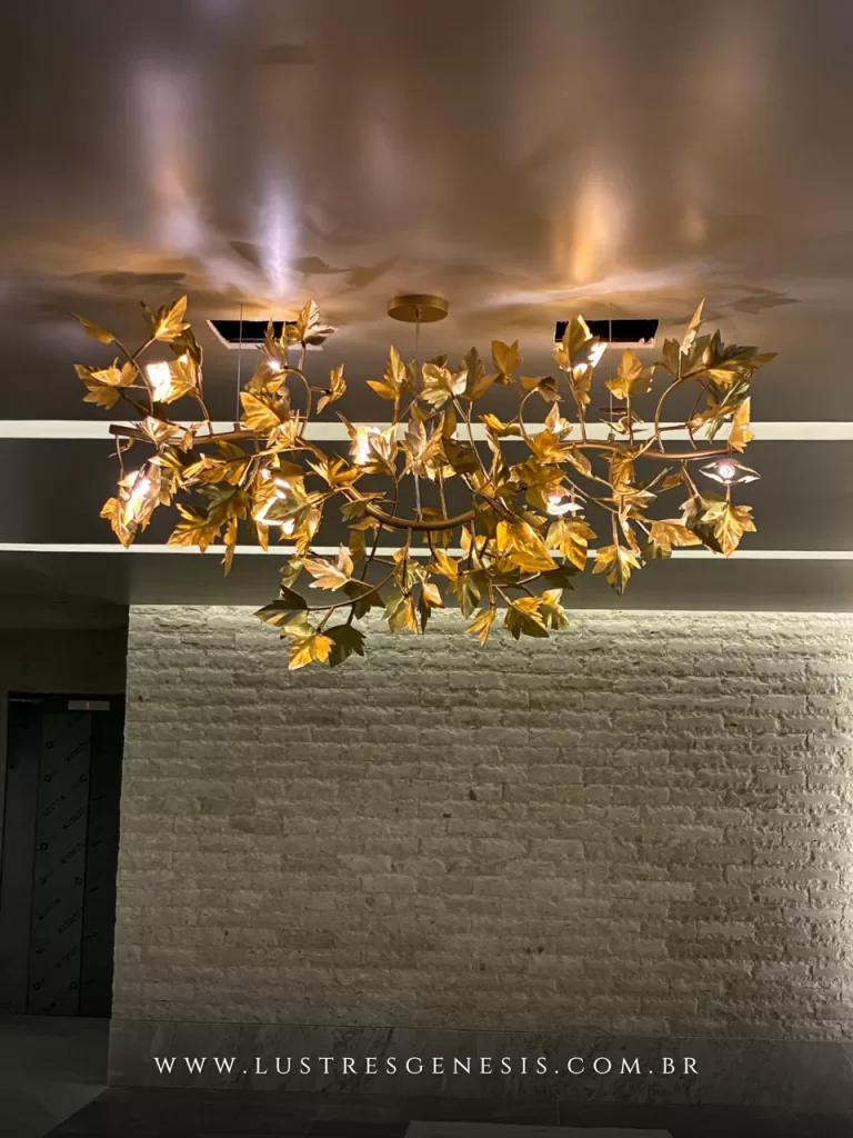 Lustre moderno dourado com design orgânico em formato de galhos e folhas metálicas, iluminando ambiente sofisticado com parede em pedra natural e luz indireta no teto, ideal para projetos de alto padrão e decoração contemporânea elegante.