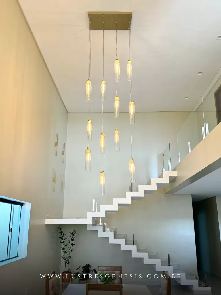 Lustre para pé-direito duplo com múltiplos pendentes tubulares em vidro transparente e LED âmbar, instalado sobre escada moderna em casa contemporânea, ideal para projetos de alto padrão com iluminação decorativa sofisticada.