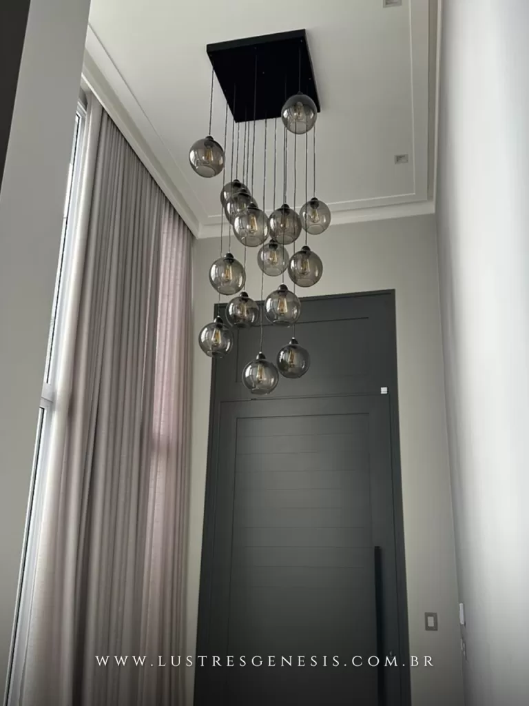 Lustre pendente com múltiplos globos de vidro fumê em diferentes alturas, instalado em hall de entrada com pé direito duplo, criando iluminação elegante e imponente.