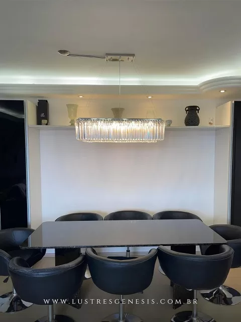 Lustre pendente de cristal retangular Bastro instalado acima de mesa de jantar preta com cadeiras modernas em ambiente sofisticado.