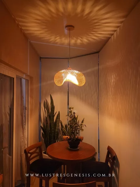 Pendente artesanal de fibra de bambu Borneu Ø60cm iluminando uma mesa redonda em área gourmet, com efeito decorativo de luz nas paredes.