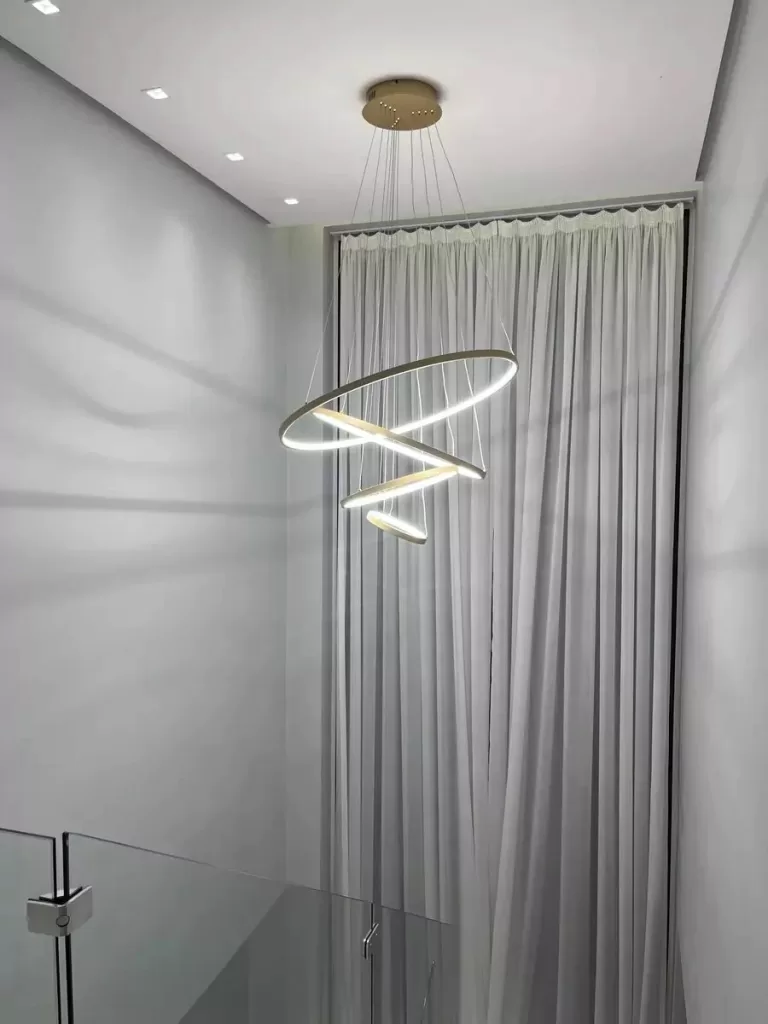 Lustre pendente moderno com design escultural em anéis assimétricos, composto por perfis de LED integrados e estrutura metálica com acabamento sofisticado. Suspenso por cabos finos reguláveis, cria um efeito leve e contemporâneo no ambiente.