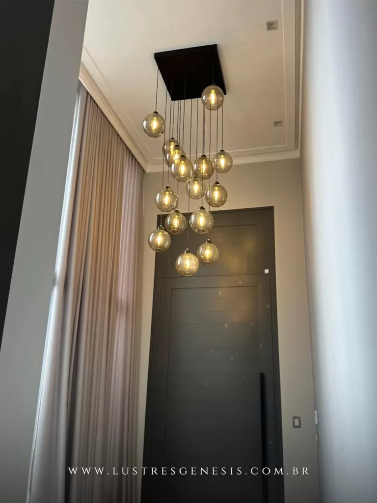 Lustre pendente Sarvah com 15 globos de vidro e base quadrada instalado em hall de entrada com pé direito duplo, iluminação moderna e elegante para ambientes altos.