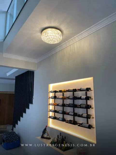 Lustre de cristal redondo Harion Ø40 transparente instalado no teto de um ambiente moderno, iluminando a sala com vinhos expostos em uma adega de parede.