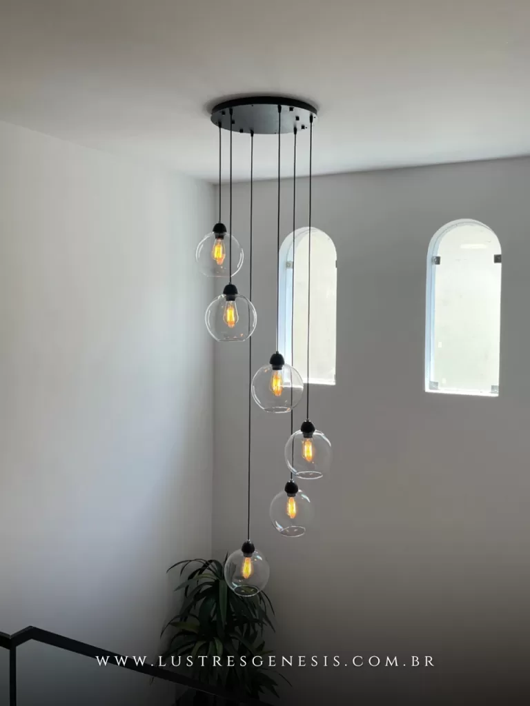 Lustre pendente Sarvah moderno com 6 globos de vidro transparente instalado em escada de casa com pé direito duplo.