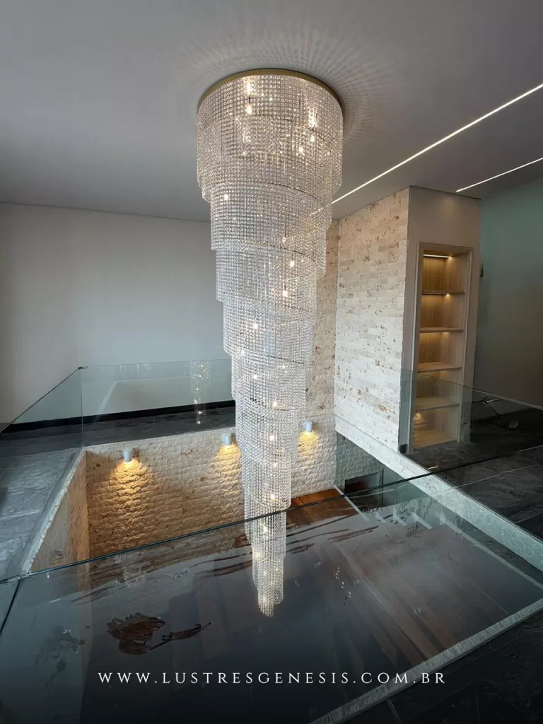 Lustre de cristal modelo cascata em formato espiral alongada, desenvolvido para ambientes com pé-direito duplo. Com estrutura metálica superior embutida no forro e múltiplas camadas de cristais lapidados, cria um efeito de queda luminosa sofisticado e imponente.Ideal para halls de entrada, escadarias e mezaninos, proporciona alto impacto visual, excelente difusão da luz e valorização arquitetônica do espaço. O design em níveis descendentes acompanha a verticalidade do ambiente, formando um elegante ponto focal decorativo.