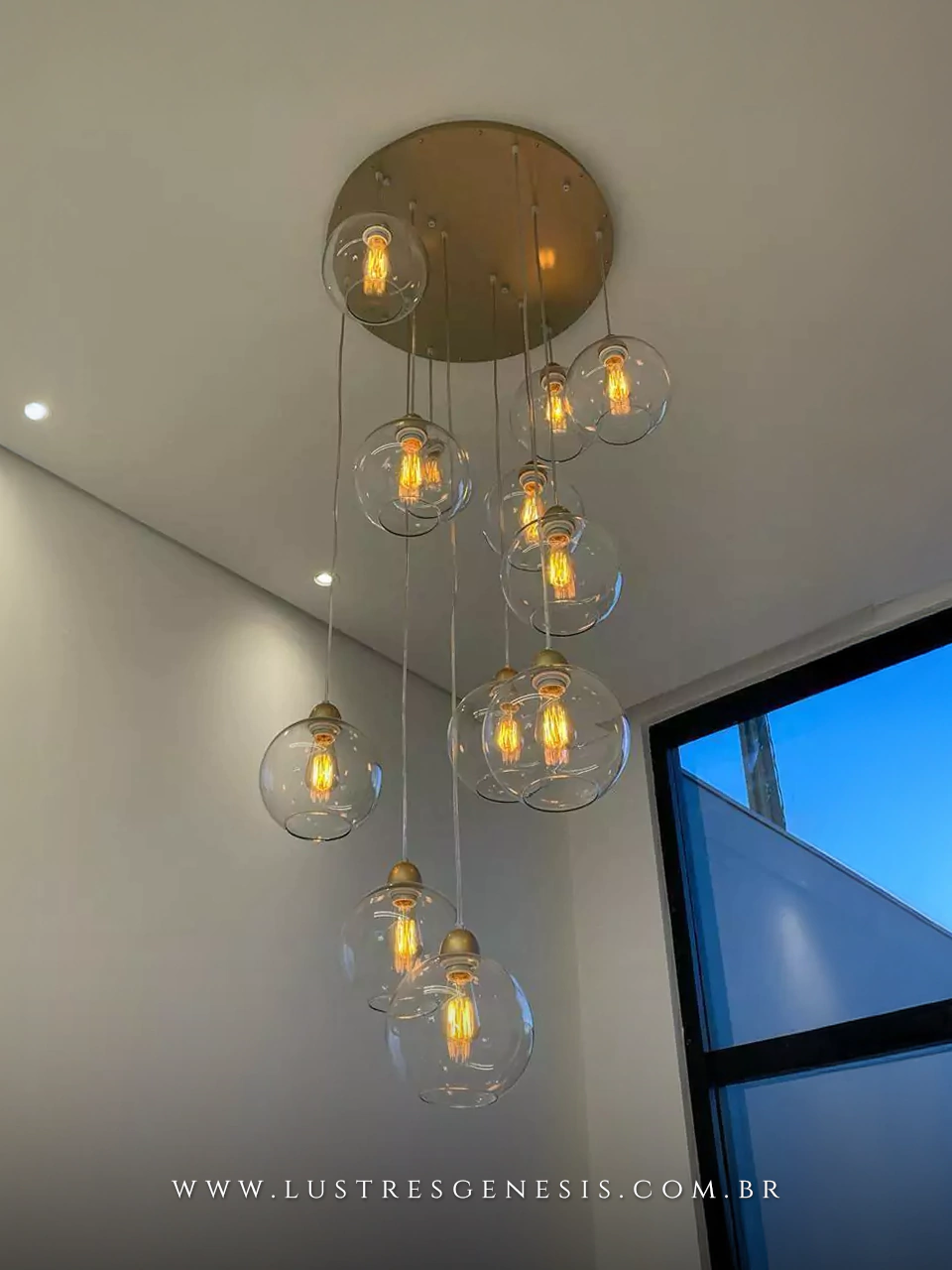 Lustre pendente Sarvah com 12 globos de vidro e base redonda preta, ideal para casas com pé direito duplo ou alto, instalado em ambiente moderno.