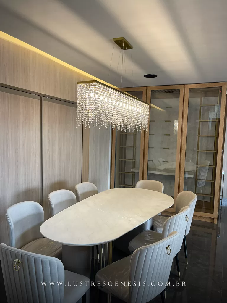 Lustre pendente retangular de cristal Fabulous 150x20 iluminando sala de jantar sofisticada com mesa oval de mármore e cadeiras estofadas.