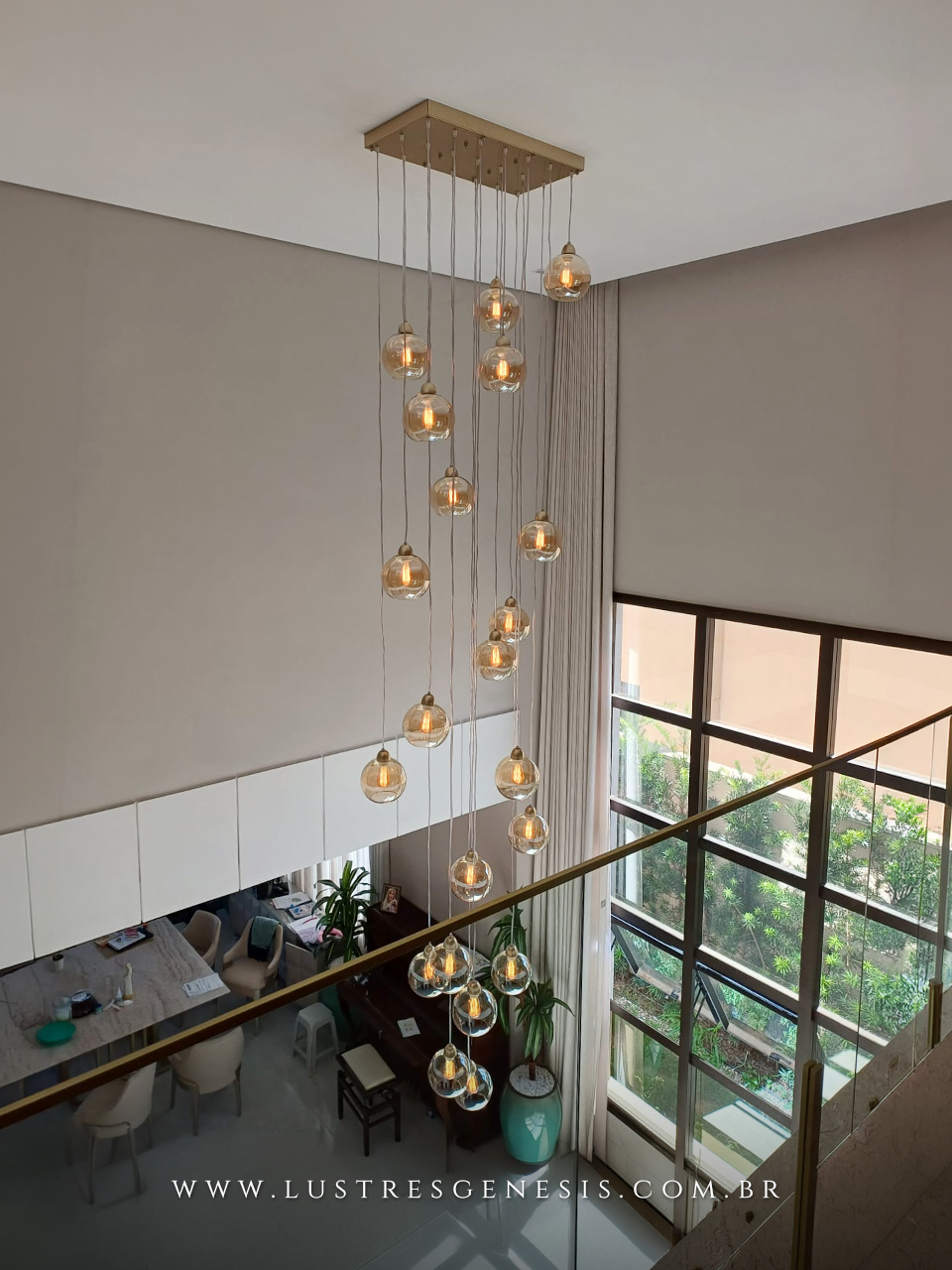 Lustre Sarvah 21 globos da Lustres Gênesis instalado em ambiente com pé direito duplo, com globos de vidro âmbar suspensos em diferentes alturas, criando efeito elegante e sofisticado com iluminação decorativa moderna.