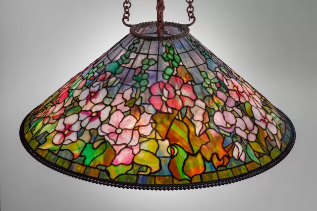 Luminária Tiffany pendente com cúpula em vitral floral colorido, apresentando flores malva em tons de rosa, branco e verde, vidro opalescente detalhado, estrutura metálica com correntes e iluminação decorativa clássica de alto valor artístico.