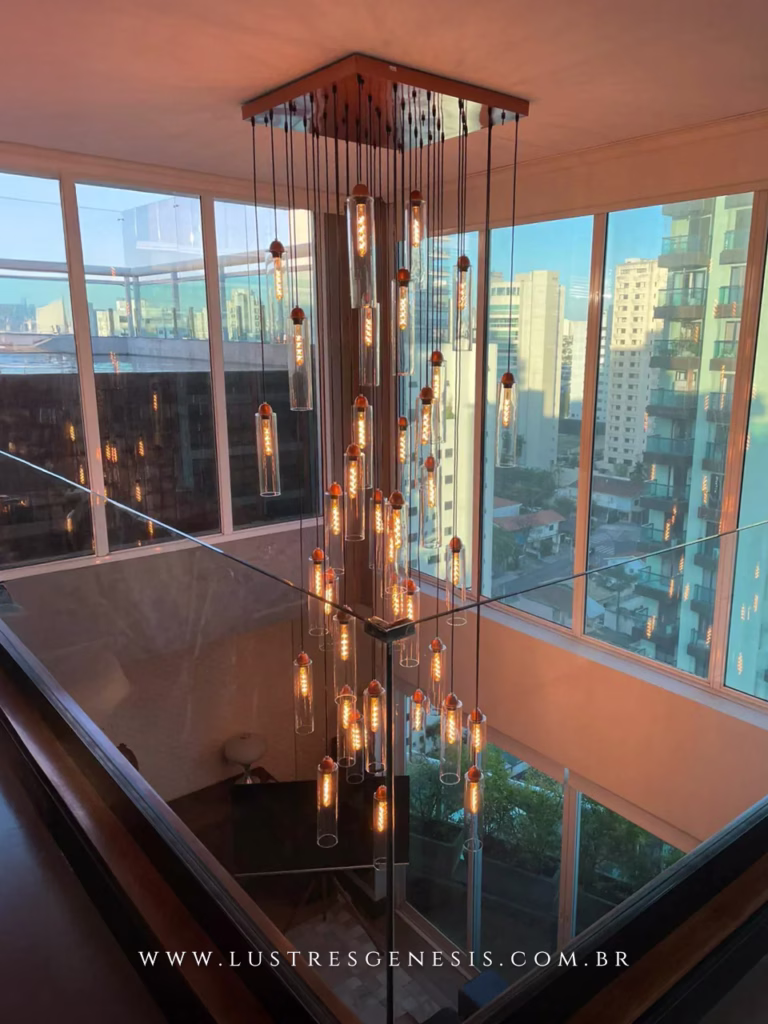 Lustre pendente moderno Dunáh com 36 tubos de vidro em base quadrada, ideal para ambientes com pé direito duplo, instalado em hall de entrada residencial sofisticado.