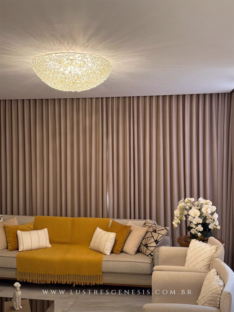 Lustre plafon de cristal modelo Cúpula Ninho Dente de Leão D80 instalado no teto de uma sala de estar elegante, com sofá bege, manta amarela e cortinas bege ao fundo.