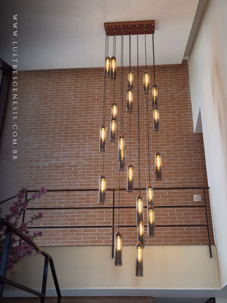 Lustre Pendente Moderno Dunáh com 21 tubos de vidro fumê e base quadrada, instalado em hall de casa com pé direito duplo, destacando iluminação sofisticada e design industrial.
