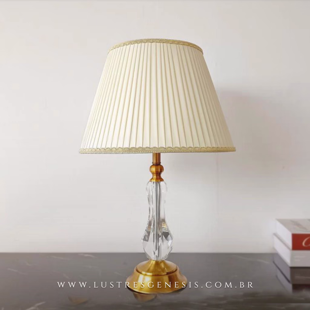 Abajur Anaia com base dourada e corpo em cristal, cúpula bege plissada, ideal para cabeceira de cama ou escritório.